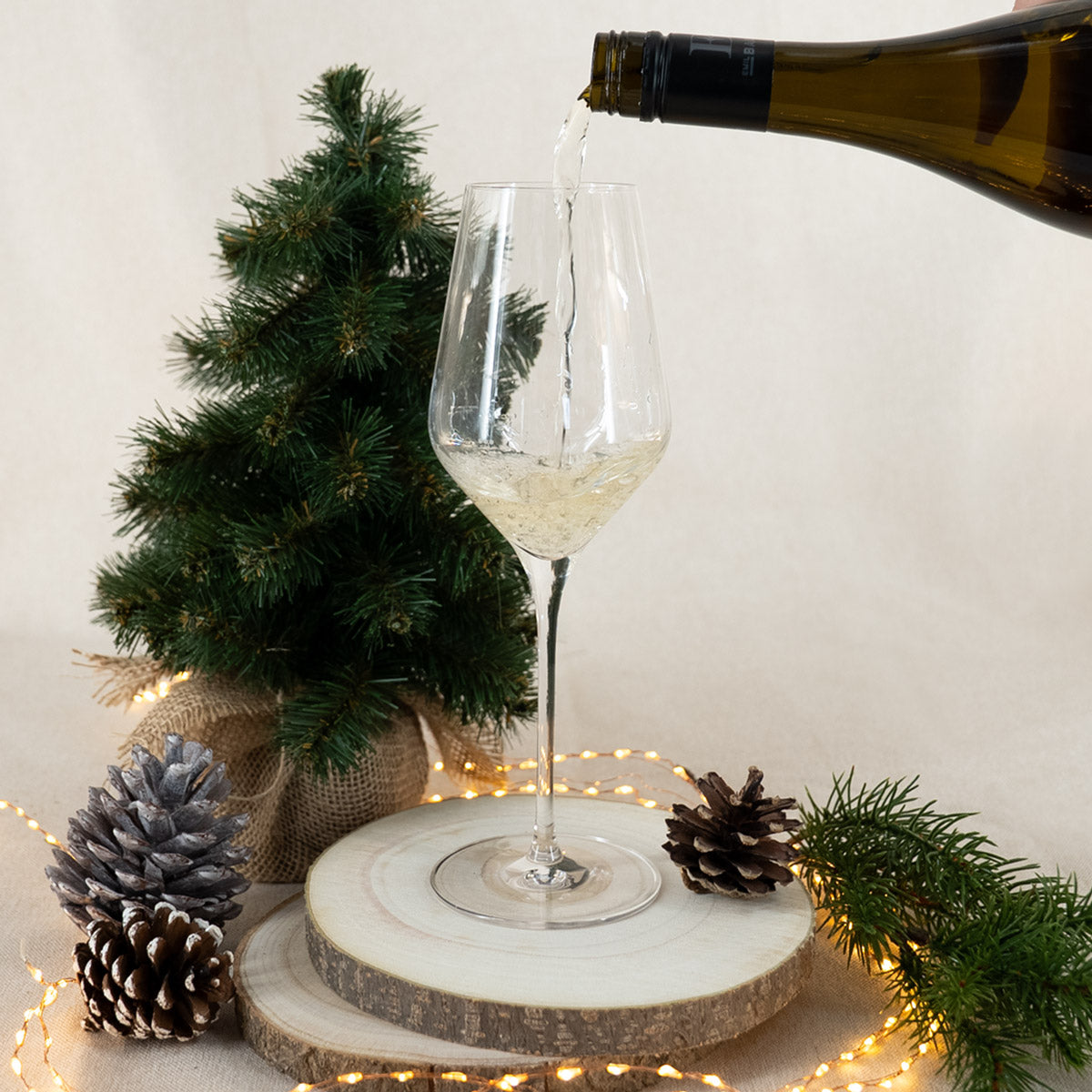 Glas Weißwein wird eingeschenkt auf Holzscheibe mit weihnachtlicher Dekoration
