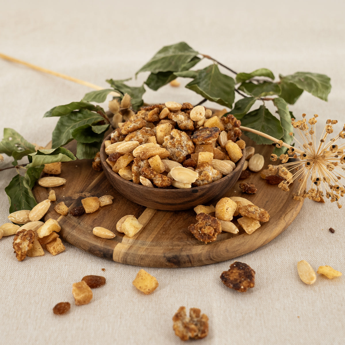 Nussmischung mit gebrannten Walnüssen, Mandeln Rosinen und Apfel-Zimt-Stückchen in einer Holzschale und herbstlicher Deko