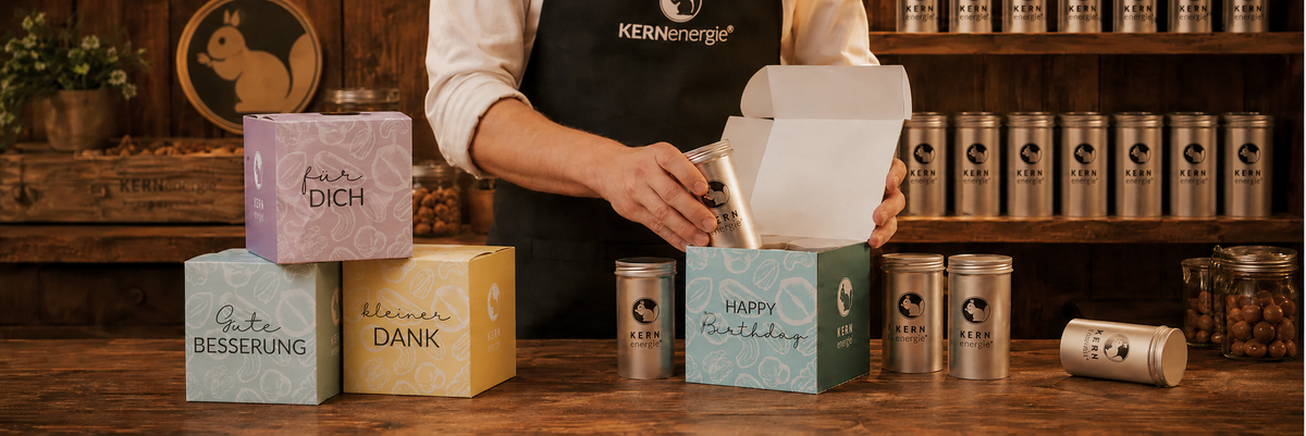 Verschiedene Mottogeschenkboxen auf einem Holztisch werden mit KERNenergie Nussdosen befüllt.
